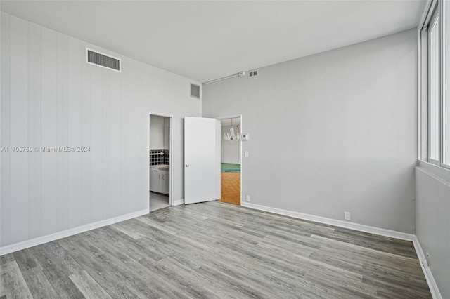 unfurnished bedroom featuring a notable chandelier, ensuite bath, and light hardwood / wood-style flooring