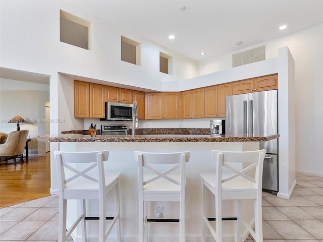 kitchen featuring a kitchen bar, a towering ceiling, stainless steel appliances, and light tile patterned floors