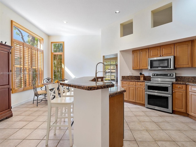 kitchen with a kitchen breakfast bar, sink, dark stone countertops, light tile patterned floors, and appliances with stainless steel finishes