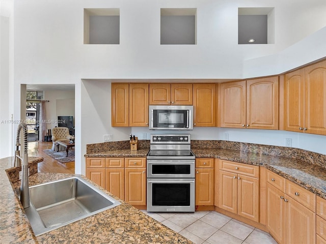 kitchen featuring dark stone counters, sink, a towering ceiling, light tile patterned floors, and stainless steel appliances