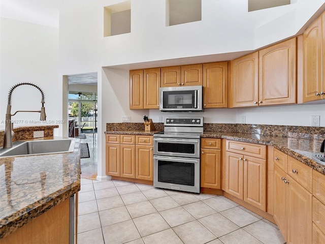 kitchen with sink, stainless steel appliances, a high ceiling, dark stone countertops, and light tile patterned floors