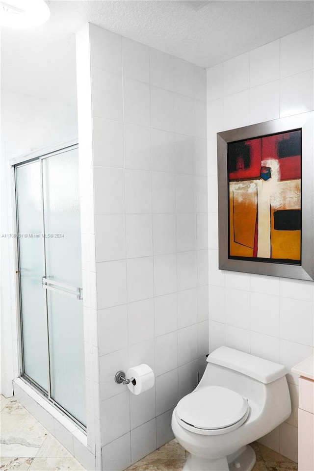 bathroom with a textured ceiling, a shower with shower door, tile walls, and toilet