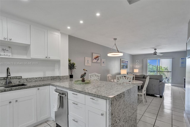 kitchen with white cabinets, open floor plan, a peninsula, light stone countertops, and a sink