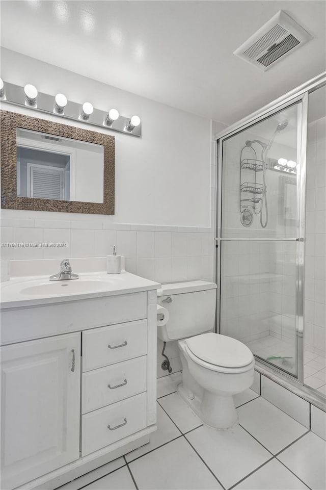 bathroom featuring tile patterned floors, an enclosed shower, toilet, vanity, and tile walls