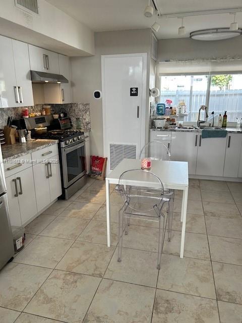 kitchen with under cabinet range hood, stainless steel range with gas cooktop, visible vents, and white cabinets