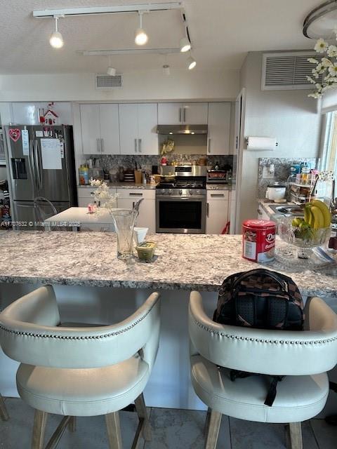 kitchen with a breakfast bar, stainless steel appliances, visible vents, decorative backsplash, and under cabinet range hood