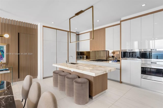 kitchen with white cabinets, sink, light tile patterned floors, and a kitchen island with sink