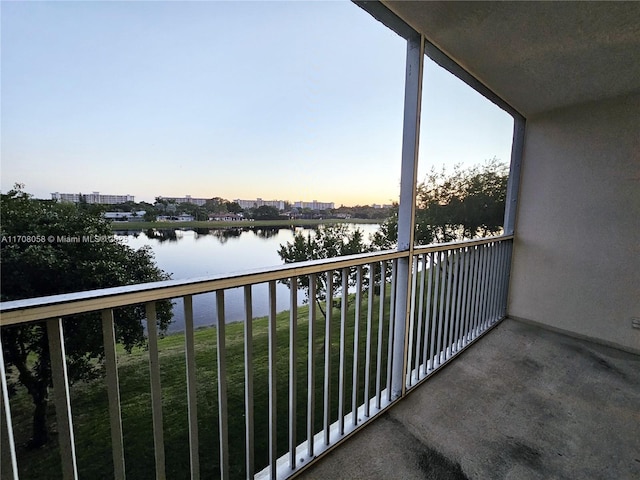 balcony at dusk featuring a water view