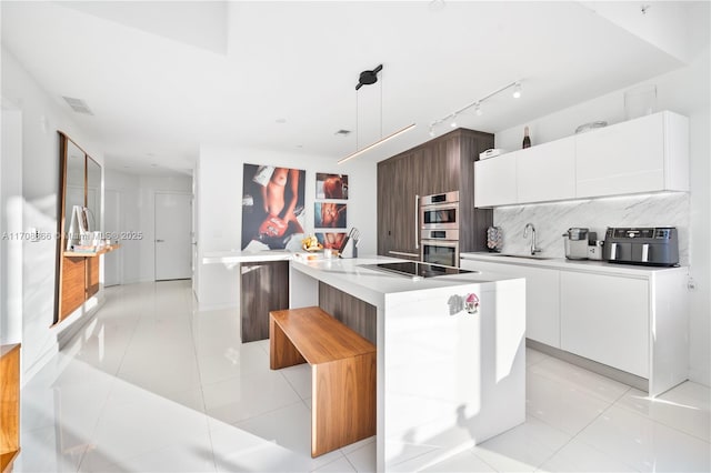 kitchen with hanging light fixtures, double oven, an island with sink, black electric cooktop, and white cabinets