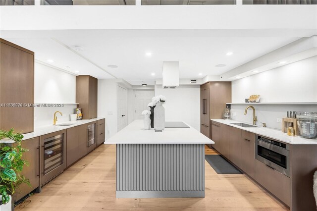 kitchen with light hardwood / wood-style floors, a kitchen island, sink, and wine cooler