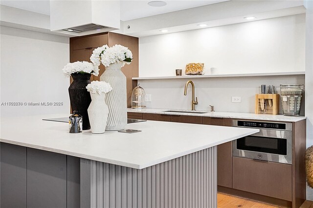 kitchen featuring sink, oven, custom range hood, and light hardwood / wood-style flooring