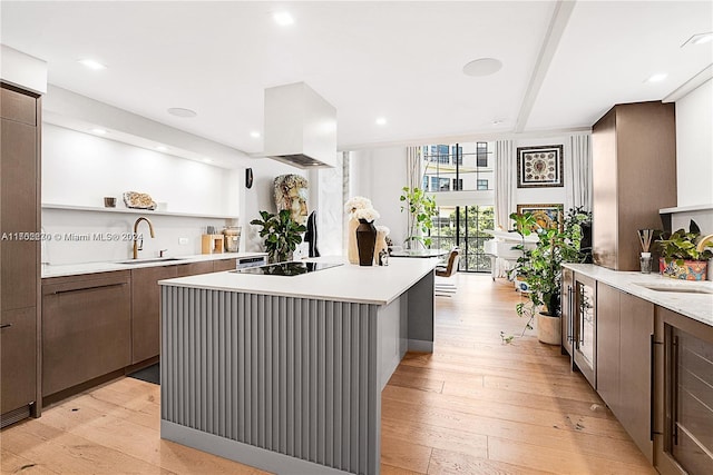 kitchen with black electric stovetop, a kitchen island, light wood-type flooring, and sink