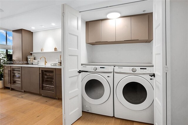 clothes washing area with cabinets, light wood-type flooring, washing machine and dryer, and beverage cooler