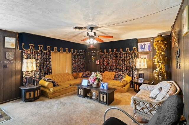 carpeted living room with a textured ceiling, ceiling fan, and wooden walls