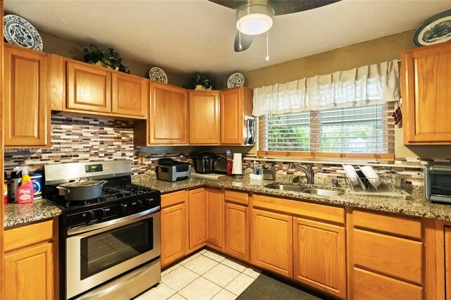 kitchen with light stone counters, ceiling fan, sink, light tile patterned floors, and stainless steel gas stove