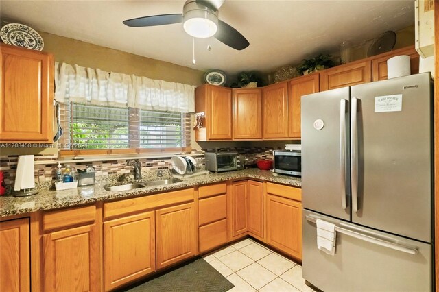 kitchen with light stone countertops, sink, ceiling fan, stainless steel appliances, and light tile patterned floors