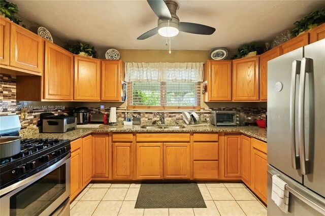 kitchen featuring sink, light tile patterned floors, dark stone counters, and appliances with stainless steel finishes