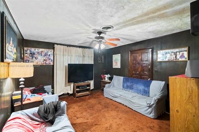 living room featuring dark colored carpet, ceiling fan, a textured ceiling, and wooden walls