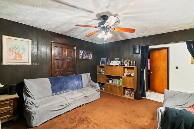 carpeted living room with ceiling fan, wood walls, and a textured ceiling
