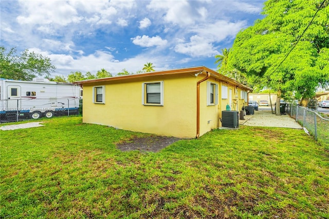 rear view of house featuring central AC, a fenced backyard, stucco siding, and a yard