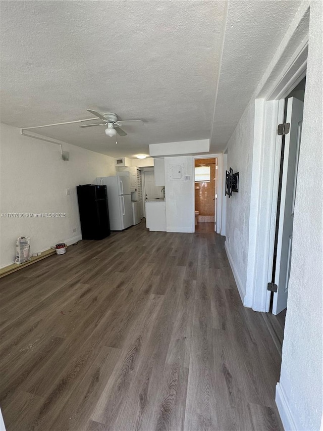 unfurnished living room with a textured ceiling, ceiling fan, dark wood-style flooring, and baseboards