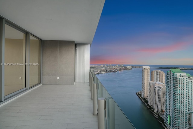 balcony at dusk featuring a water view