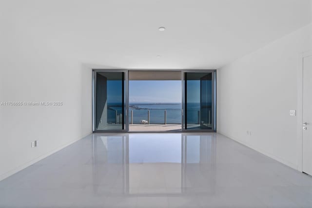 tiled spare room featuring a water view, plenty of natural light, and expansive windows