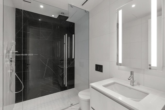 bathroom with vanity, a tile shower, tile walls, and toilet