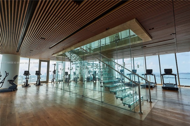 gym featuring hardwood / wood-style floors, a wall of windows, and a water view