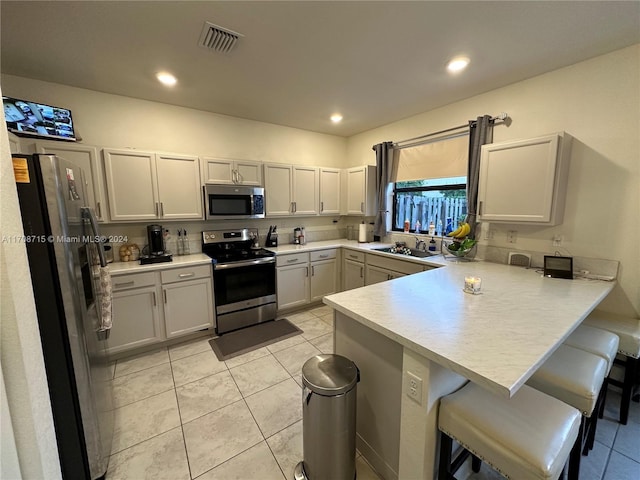 kitchen with kitchen peninsula, stainless steel appliances, sink, light tile patterned floors, and a breakfast bar area