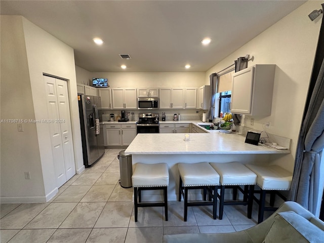 kitchen featuring sink, light tile patterned floors, appliances with stainless steel finishes, kitchen peninsula, and a breakfast bar area