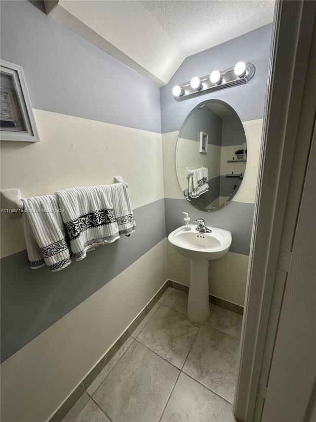 bathroom featuring tile patterned flooring, lofted ceiling, and a textured ceiling