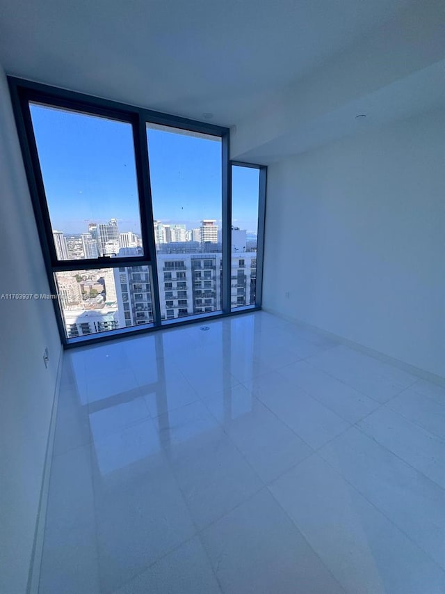 empty room with tile patterned flooring, a wall of windows, and a healthy amount of sunlight