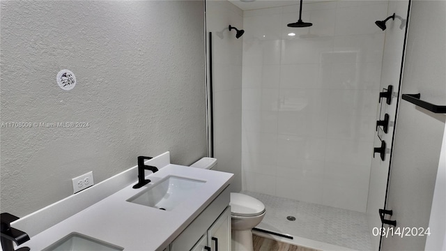 bathroom with a tile shower, vanity, hardwood / wood-style flooring, and toilet