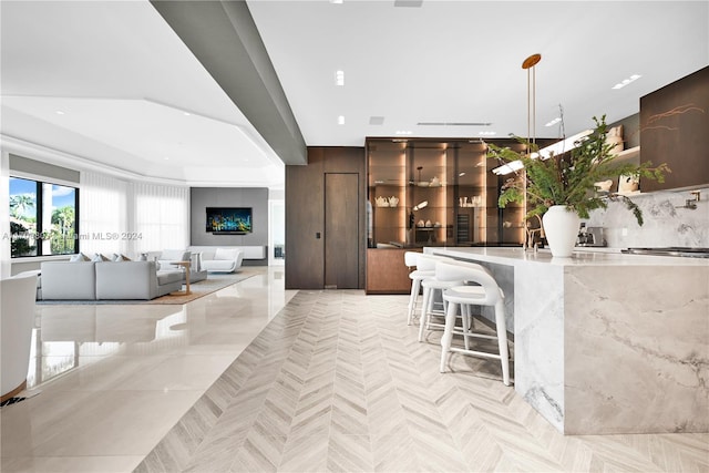 kitchen featuring pendant lighting, a kitchen breakfast bar, decorative backsplash, light stone countertops, and a tray ceiling