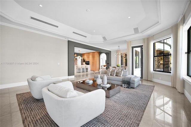 tiled living room featuring a notable chandelier, ornamental molding, and a tray ceiling