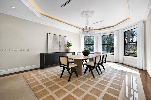 dining area with light wood-type flooring, a tray ceiling, crown molding, and a notable chandelier