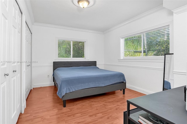 bedroom featuring light wood-type flooring, crown molding, and multiple windows