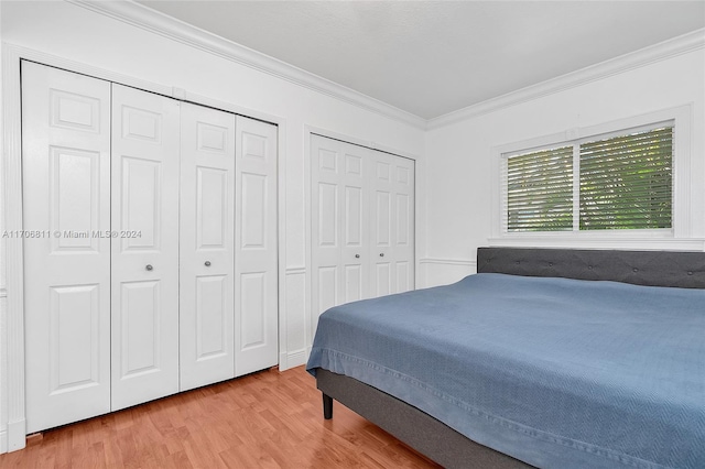 bedroom featuring multiple closets, ornamental molding, and light wood-type flooring