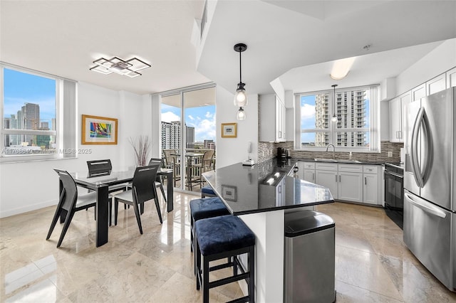 kitchen featuring stainless steel fridge, white cabinetry, backsplash, a kitchen breakfast bar, and decorative light fixtures