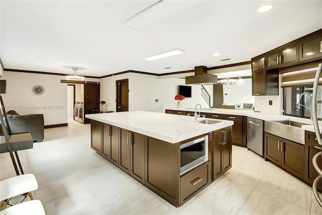 kitchen with sink, dark brown cabinets, a center island with sink, stainless steel appliances, and light stone countertops