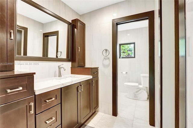 bathroom with tile walls, vanity, tile patterned flooring, and toilet