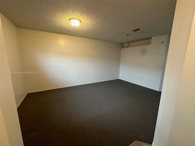 empty room featuring dark carpet and a textured ceiling