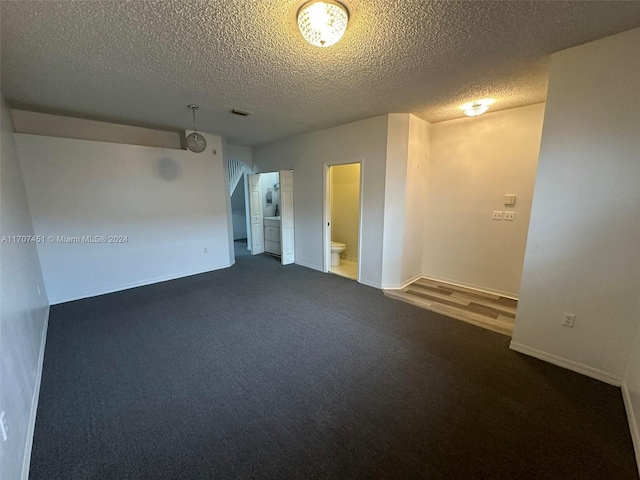 unfurnished room featuring a textured ceiling and dark carpet