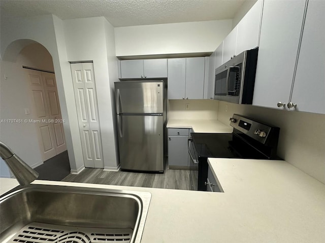 kitchen featuring sink, hardwood / wood-style flooring, a textured ceiling, white cabinetry, and stainless steel appliances