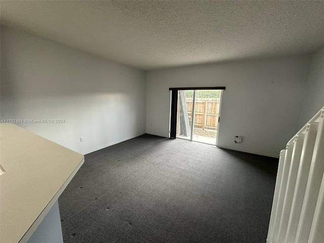 spare room with dark carpet and a textured ceiling