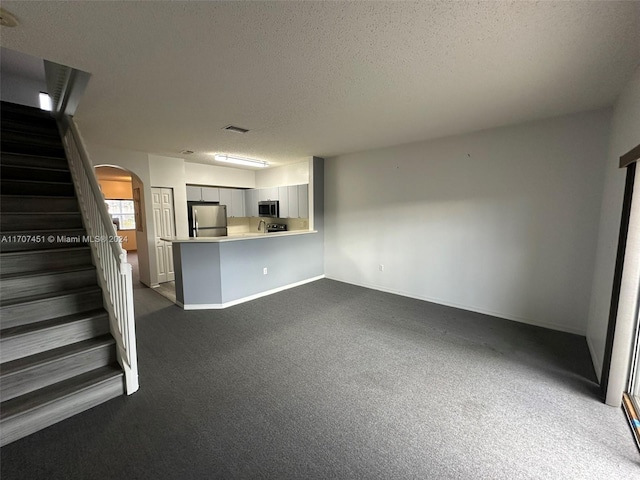 unfurnished living room featuring dark colored carpet and a textured ceiling