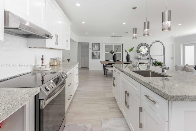 kitchen featuring pendant lighting, an island with sink, exhaust hood, stainless steel electric range, and sink