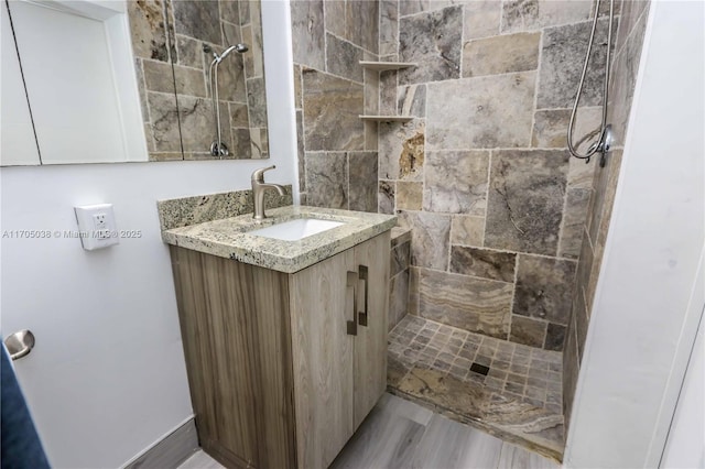 bathroom with tiled shower, vanity, and wood-type flooring