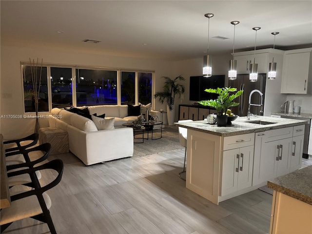 kitchen with an island with sink, light wood-type flooring, a breakfast bar area, white cabinetry, and sink